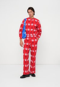 Felpa con motivo floreale rosso e pantaloni abbinati, realizzati in tessuto morbido, abbinati a una borsa a tracolla blu. Scarpe nere completano l'outfit.