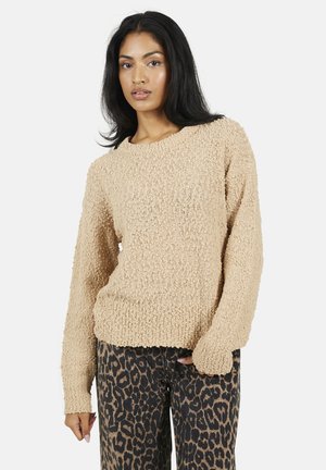 Beige gebreide trui met een ronde hals en lange mouwen, gecombineerd met een broek met luipaardprint. De trui heeft een losse pasvorm.
