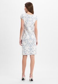 Besticktes Kleid in Hellblau mit weißem Blumenmuster. Kurze Ärmel, taillierte Form, gewellter Saum, kombiniert mit silbernen Riemchenschuhen.