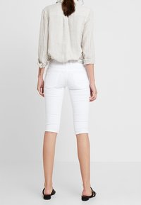 Jeans blancos cortos con un diseño ajustado, textura suave y dos bolsillos traseros. Combinados con una camisa de lino ligera.