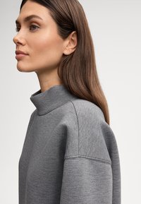 Grijze sweatshirt met mock-neck, featuring een zachte textuur, verlaagde schouders en een subtiel heatherpatroon. De stof heeft een gladde afwerking.