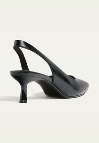 Črne slingback pete s koničastim nosom, narejene iz strukturirane usnje. Imajo elegantno, zoženo peto in izrezljan vzorec ob straneh.