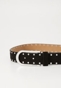 Mustat mokkataskuvyö, jossa on hopeanvärisiä metallisia pilkkuja, sileä hopeinen solki ja beige sisus, jossa on rei'itettyjä reikiä.