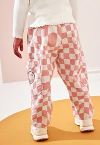Rosa och vita rutig cargobyxor med en sidoficka som har en smiley-design, kombinerat med krämfärgade sneakers.