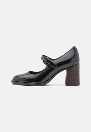 Chaussure Mary Jane en cuir verni noir avec un bout rond, une sangle réglable, des détails en métal doré et un talon en bois épais.