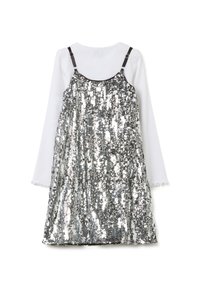 Vestido de lentejuelas plateadas sin mangas con un diseño de tirantes negros, superpuesto a una blusa blanca de manga larga con puños volantes.