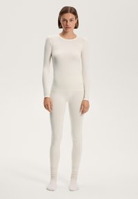 Top termico a maniche lunghe, aderente, e leggings in morbido tessuto bianco. Texture liscia, con colletto a giro e polsini a coste.