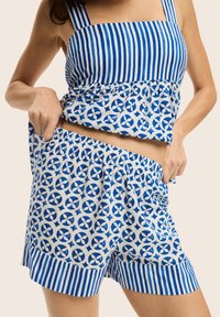Zestaw z niebieską i białą wzorzystą bluzką na krótki rękaw i szortami, z paskami i okrągłymi motywami. Miękka tkanina z elastycznym wykończeniem w talii.