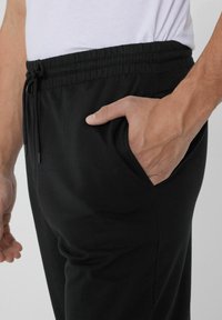 Zwarte joggers met een elastische tailleband, trekkoorddetails en zijzakken. Glad materiaal met een taps toelopend ontwerp.
