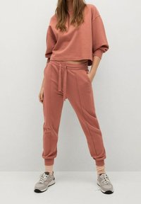 Różowy skrócony sweter i pasujące spodnie dresowe z wiązaniem w pasie. Miękki materiał, ściągacze na rękawach i szczegóły przy bocznych szwach. Sportowe tenisówki.