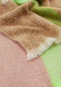 Couverture en laine d'un mélange de sections marron, beige doux et rose pastel avec une texture duveteuse, et un bord frangé blanc.