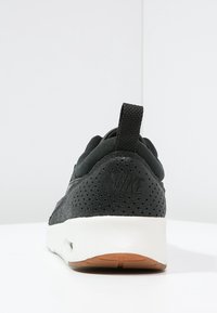 Svart sneaker med en texturerad överdel, perforeringar för andningsförmåga och en vit sula. Har en dragöppning och logotyp på hälen.