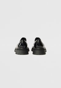Black patent leather shoes with decorative stitching, a chunky black rubber sole, and a smooth texture. Viewed from the back.