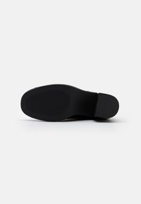 La suola nera della scarpa presenta una superficie liscia, leggermente texturizzata, con scanalature orizzontali per una migliore aderenza. Tacco arrotondato e design minimalista.