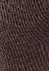 Gros plan sur un tissu brun avec une texture froissée et ondulée s’étendant verticalement sur la surface.