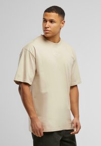 Short-sleeved beige t-shirt made of cotton, featuring a subtle white logo on the chest. Regular fit with a round neckline and smooth texture.
