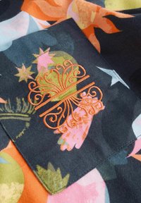 Mustast kangast koosnevad erkroosade, oranžide ja roheliste lillemustritega. Keskel oranž tikand, millel on keerukad keerutused ja jooned.