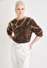 Suéter esponjoso marrón y beige con un diseño de estampado animal, combinado con jeans blancos de cintura alta que presentan detalles en cobre.