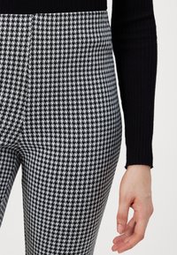 Zwart-wit pied-de-poule geprinte broek met een getailleerd ontwerp, gemaakt van een gestructureerd materiaal, gecombineerd met een zwart geribbeld top.