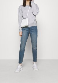 Felpa grigia chiara in pile con collo rotondo, jeans in denim blu e sneakers bianche. Una piccola borsa bianca a tracolla è indossata come crossbody.