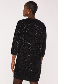 Abito nero di paillettes con maniche a tre quarti, tessuto strutturato, scollo rotondo e bordi rifiniti, che mostra un motivo scintillante.