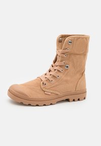 Botas de tobillo de lona color beige con una superficie texturizada, puntera de goma contrastante y ojales de metal para los cordones, con una suela robusta y con relieve.