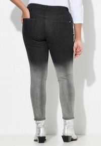 Jeans de mezclilla ombré de negro a gris con un diseño ajustado, bolsillos traseros y puños terminados, combinados con botas de tobillo plateadas y brillantes.