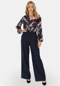 Wielokolorowa bluzka w kwiaty z długimi rękawami, granatowe spodnie z wysokim stanem oraz czarne szpilki. Bluzka ma kołnierzyk i błyszczącą teksturę.