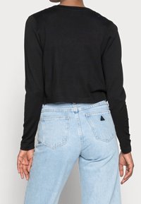 Haut noir à manches longues et court, associé à un jean taille haute bleu clair, avec des poches arrière et un petit logo triangle sur la poche droite.