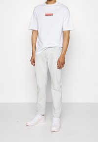 Biała koszulka z krótkim rękawem z czerwonym nadrukiem, zestawiona z jasnoniebieskimi dżinsami i białymi trampkami z różowymi akcentami. Minimalistyczny design.