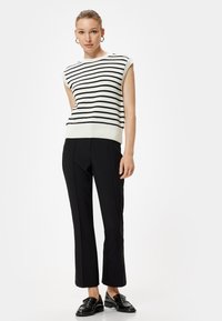 Wit en zwart gestreepte gebreide trui met korte mouwen, gecombineerd met nauwsluitende zwarte broek en zwarte instappers. Glad textuur, casual pasvorm.