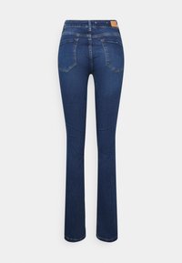 Jeans de campana azul oscuro con una textura de denim suave, que presentan dos bolsillos traseros y un parche de cuero marrón en la cintura.