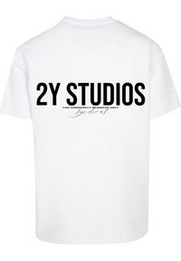 Bílý bavlněný tričko s odvážným černým textem na zadní straně: "2Y STUDIOS POUZE PRO ČLENY KOMUNITY" s kurzívou pod ním.
