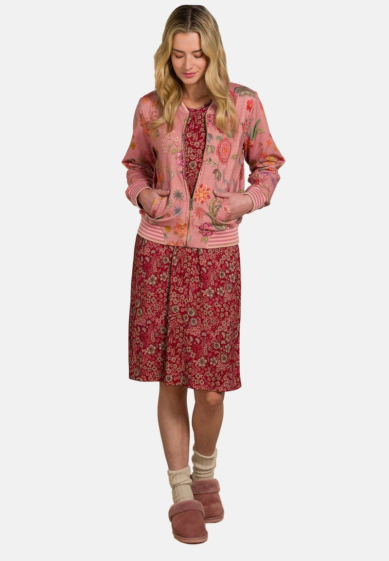 Pink bomber jacket with floral embroidery over a red floral dress. Worn with cream socks and pink fur-lined slippers.