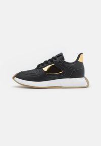 Sneaker nera con accenti dorati, dotata di tomaia in pelle liscia, punta arrotondata e suola bianca spessa con finitura texturizzata.