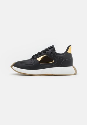 Černé tenisky se zlatými akcenty, s hladkým koženým svrškem, zaoblenou špičkou a silnou bílou podrážkou s texturovaným povrchem.