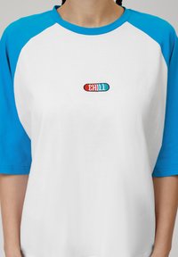 Valge puuvillane T-särk siniste raglanvarrukatega. Keskel rinnas on edev "CHILL" logo, millel on punase ja türkiissinise tikandi detailid.