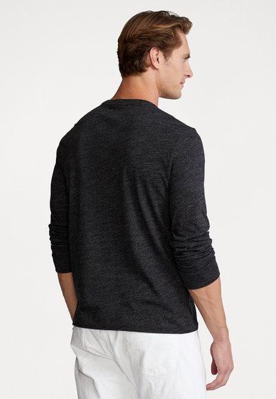 Lange mouwen, donkergrijze t-shirt gemaakt van een zachte, gestructureerde stof. Heeft een ronde hals en opgerolde mouwen, gecombineerd met witte shorts.