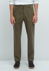 Chinos kaki avec une texture lisse, design à jambe droite et deux poches latérales. Associés à des chaussures à lacets marron foncé.