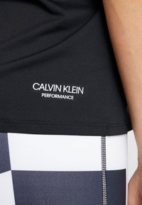 Zbliżenie osoby ubranej w czarny top Calvin Klein Performance oraz czarne legginsy w biało-szaro-czarną kratę.
