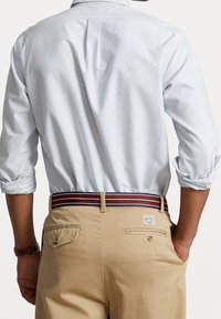 lichtblauw en wit gestreepte shirt met opgerolde mouwen, gedragen met tan broek en een veelkleurige gestreepte riem met een label.