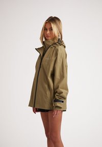Giacca impermeabile verde oliva con cappuccio, zip frontale e polsini regolabili. Presenta un logo discreto e una texture elegante e liscia.