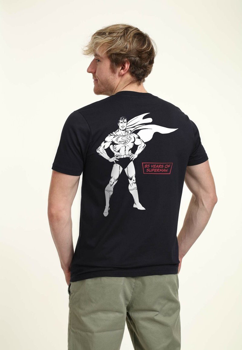 Svart bomull t-shirt med en stor vit grafik av en superhjälte på baksidan, med texten "85 år av Superman" nedanför.
