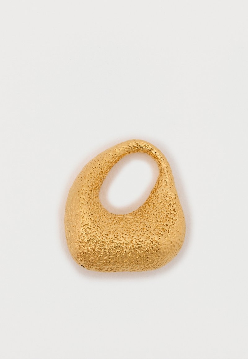 Zelta tonis metāla gredzens ar teksturētu, neregulāru formu un izgrieztu daļu. Virsma šķiet raupja un atstarojoša, uzsverot tā kontrastējošo dizainu.