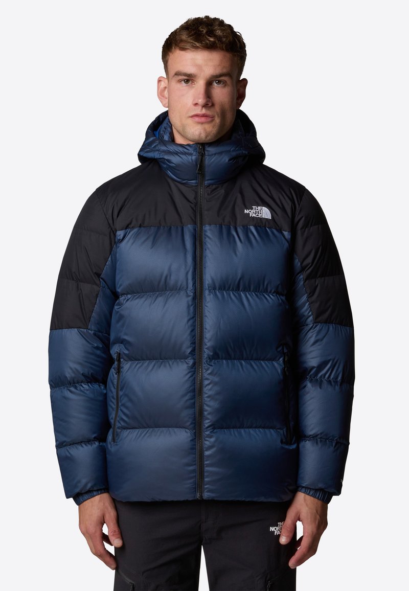 Granatowa kurtka puchowa z czarnymi akcentami, zasuwana z przodu, z kapturem. Charakteryzuje się teksturowanym, izolowanym designem oraz bocznymi kieszeniami.