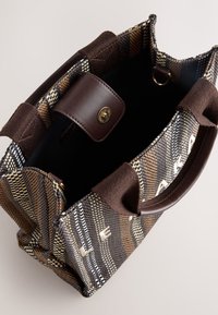 Sac à main tissé marron texturé avec des accents en cuir, présentant un intérieur spacieux, deux poignées et une fermeture à pression dorée avec détail de logo.