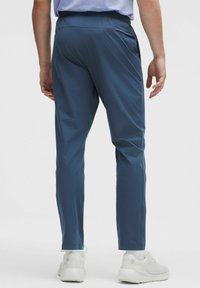 Tamsiai mėlyni techniniai sportiniai džinsai, su siaurėjančiu dizainu, tempimo medžiaga ir šoninėmis kišenėmis. Tinka aktyviam naudojimui.