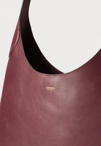 Burgundy bőr hobo táska sima textúrával, arany fémzáras márkafelirattal és egyetlen vállpánttal.