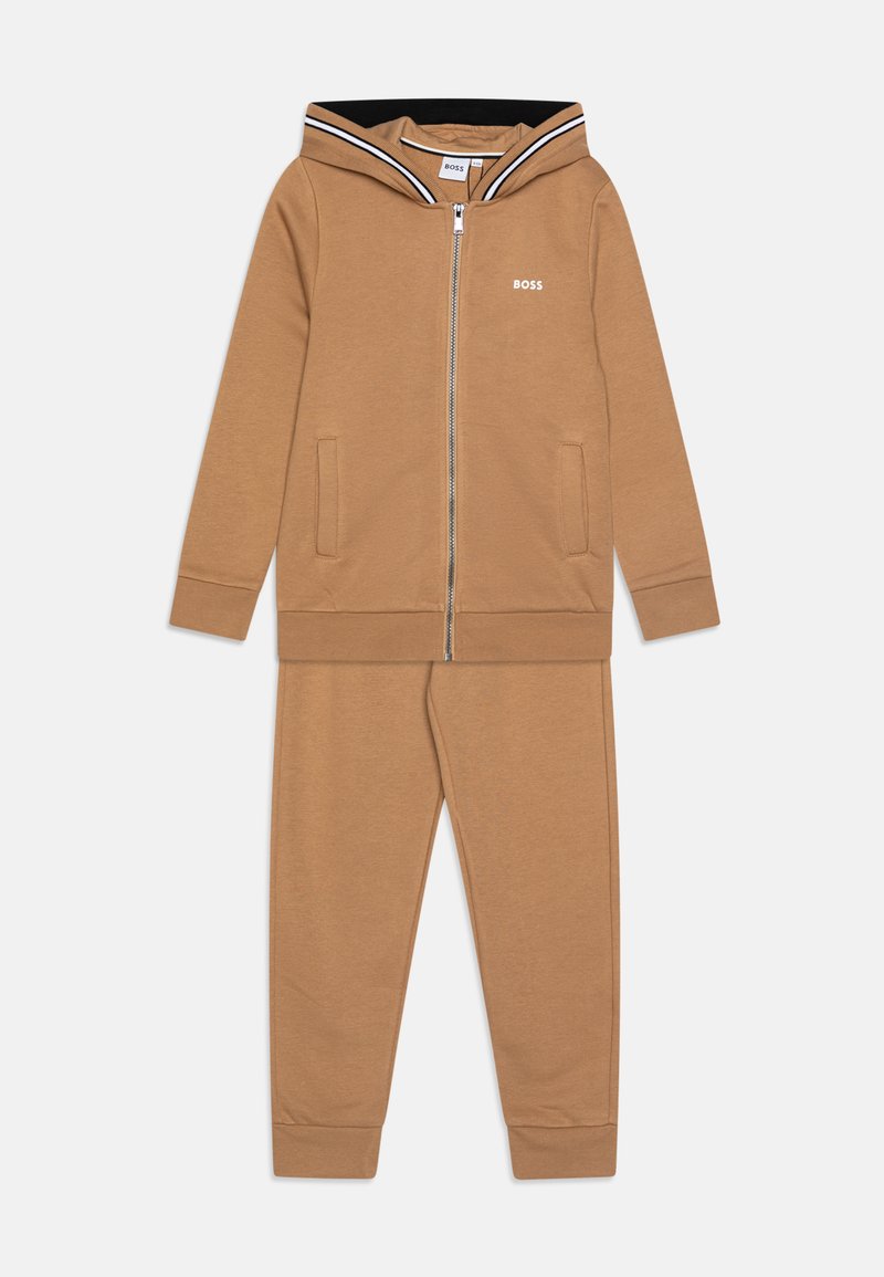 Haut à zip marron avec une capuche doublée de noir, logo blanc, et deux poches avant ; pantalon de sport marron assorti avec des poignets côtelés.