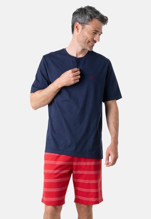 T-shirt en coton bleu marine à manches courtes avec un petit logo d'ancre rouge sur la poitrine, assortie à un short rouge avec des rayures horizontales blanches.